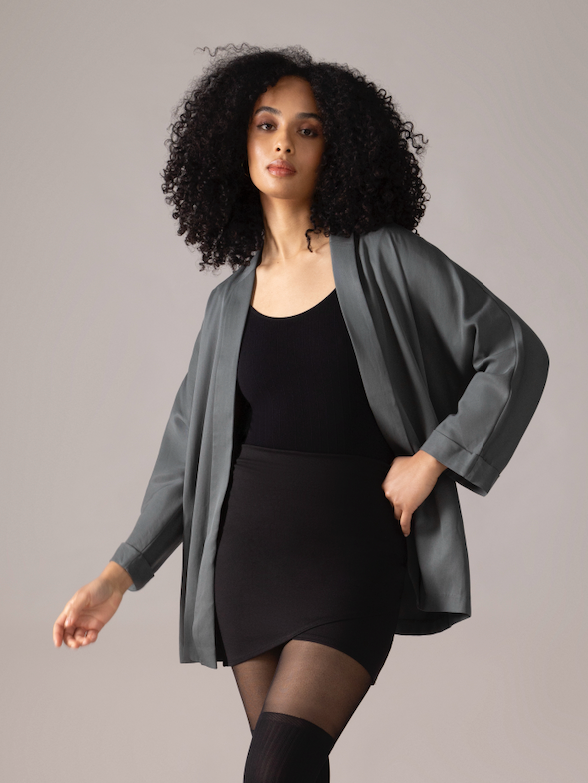Woman wearing a green kimono cardigan, black top, skirt, and knee-high boots socks