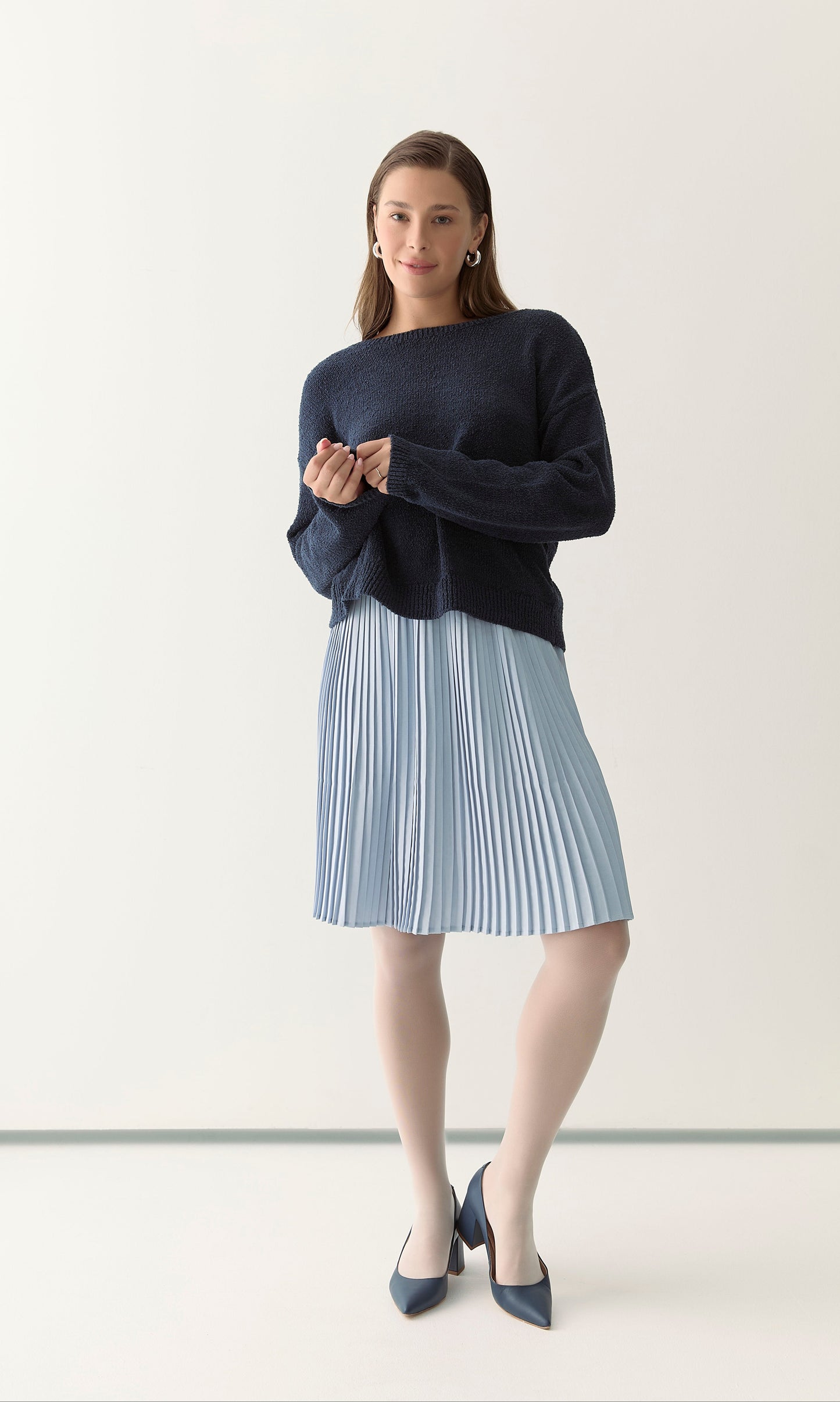 Woman wearing a navy sweater and light blue pleated skirt 