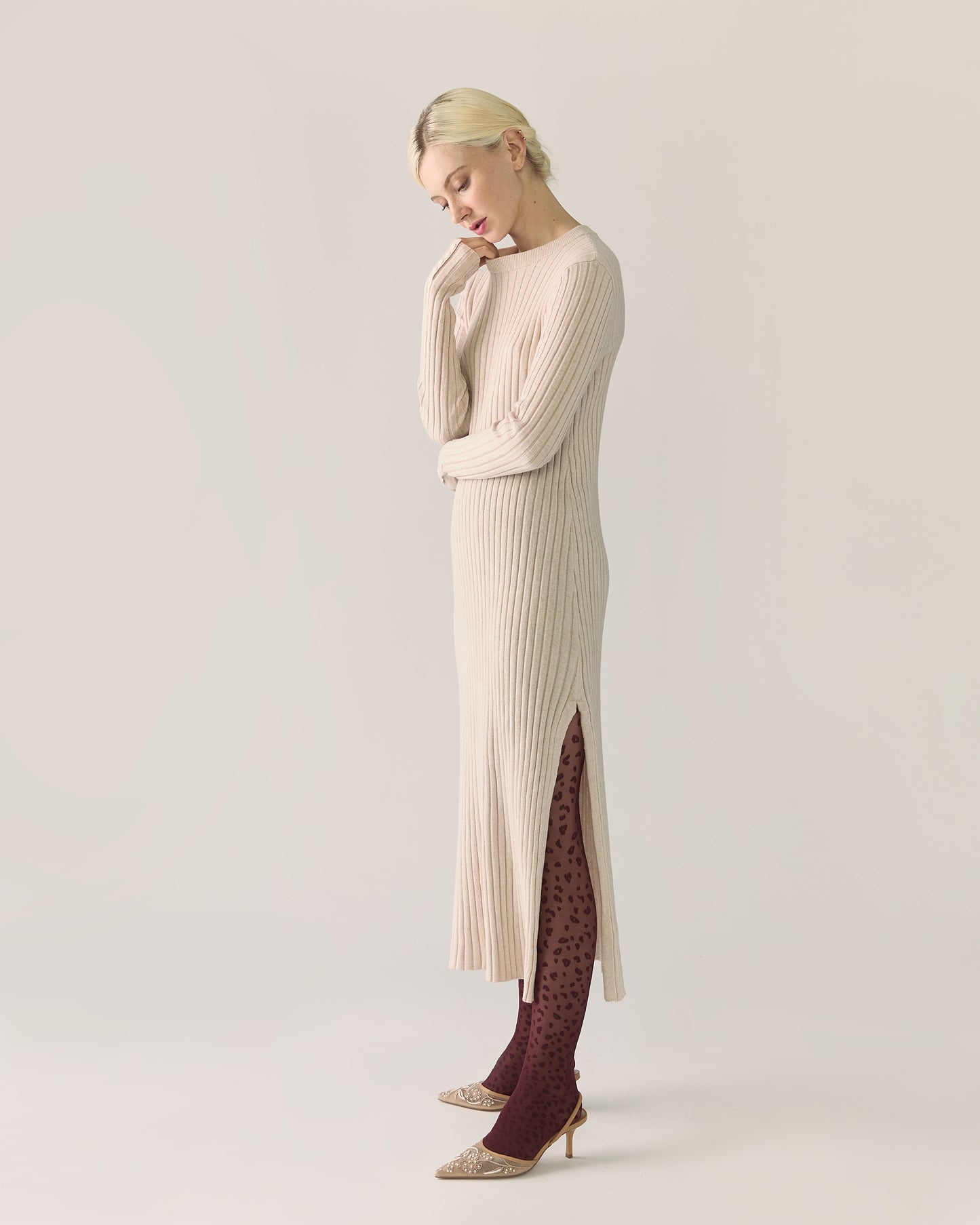 Woman wearing a long beige ribbed sweater dress with a slit
