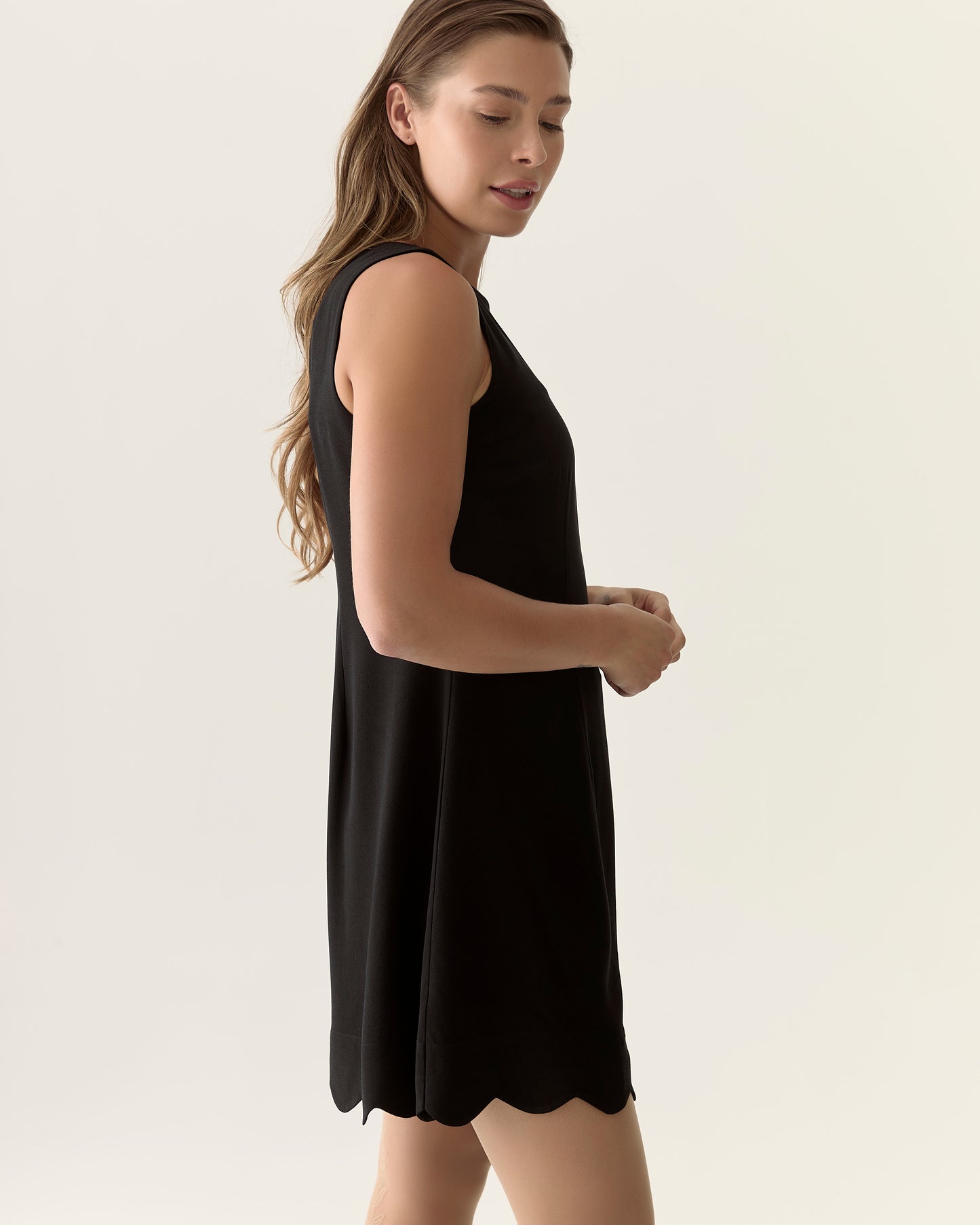 Woman wearing a black sleeveless dress against a plain background