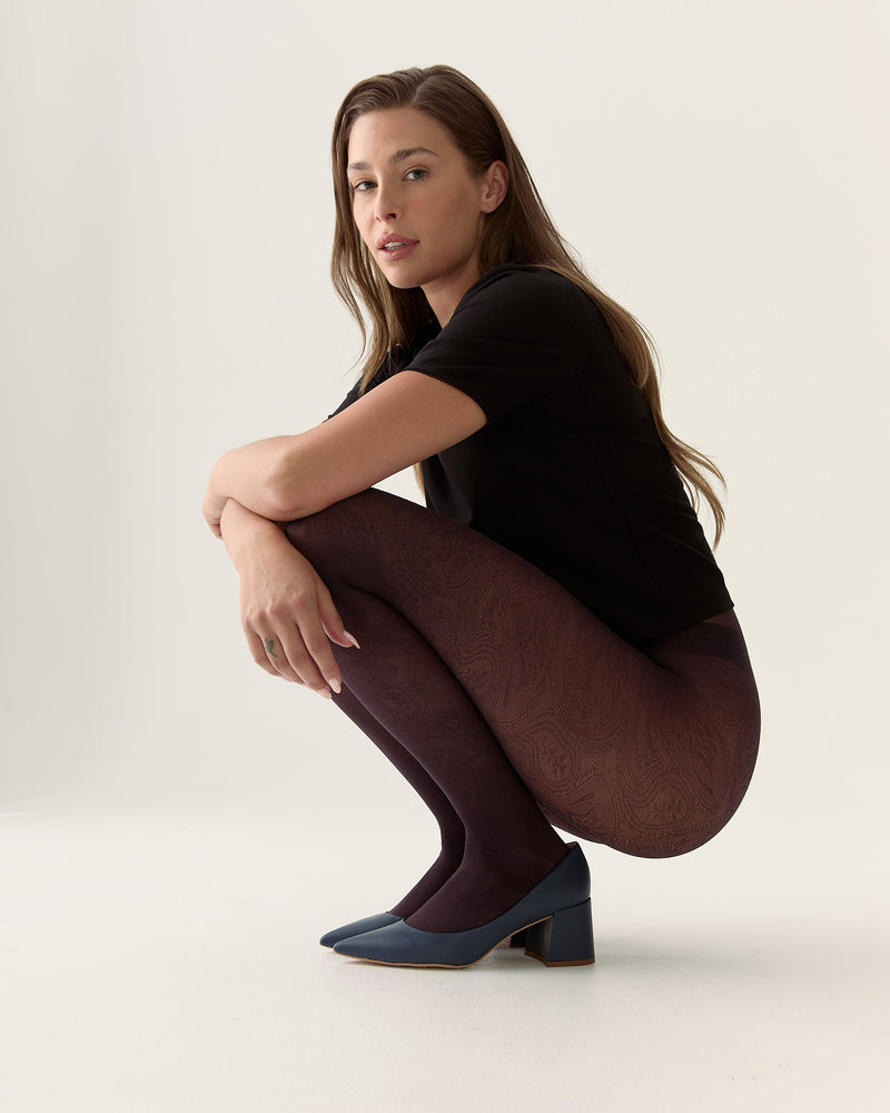 Woman wearing a black top and brown pants crouching on a light background