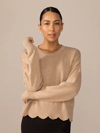 Woman wearing a beige sweater with a scalloped hem 