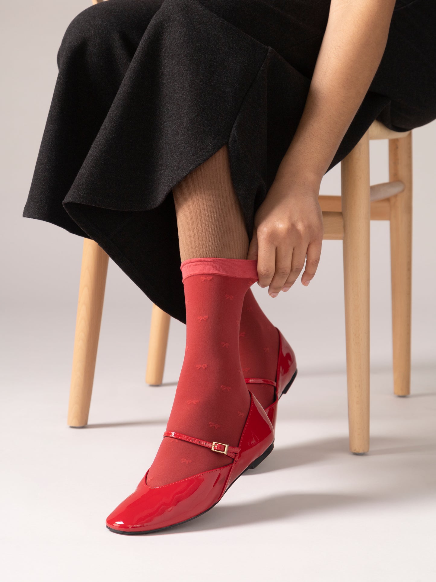 Person wearing red shoes and black pant sitting on a wooden stool.